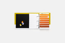 Load image into Gallery viewer, The Pantone Solid Chips Set showing an open ring binder on a light grey background. The left panel is black with three small, colourful sticky notes, and the right panel shows orange-and-white weekly strip pages.